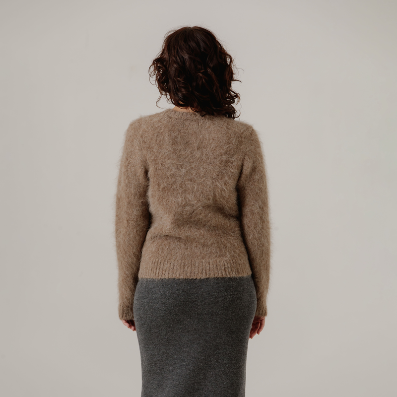 Person wearing a light brown textured sweater and gray skirt against a plain background