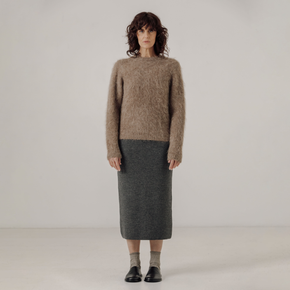 Woman wearing a light brown textured sweater and gray skirt against a plain background