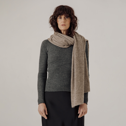 Woman wearing a gray sweater and beige scarf against a plain background