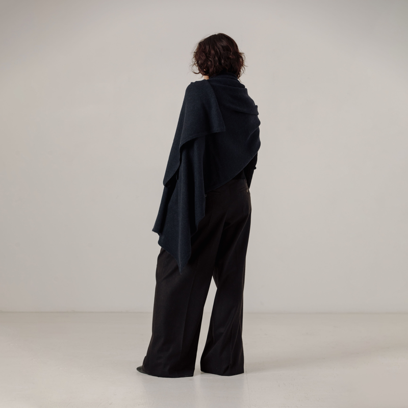 Person wearing a black outfit with a draped navy shawl on a white background