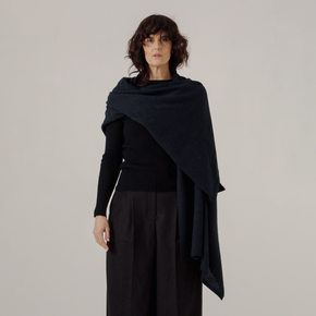 Woman wearing a dark blue shawl over a black outfit on a plain background