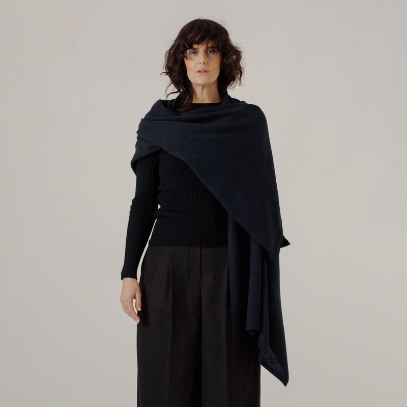 Woman wearing a dark blue shawl over a black outfit on a plain background