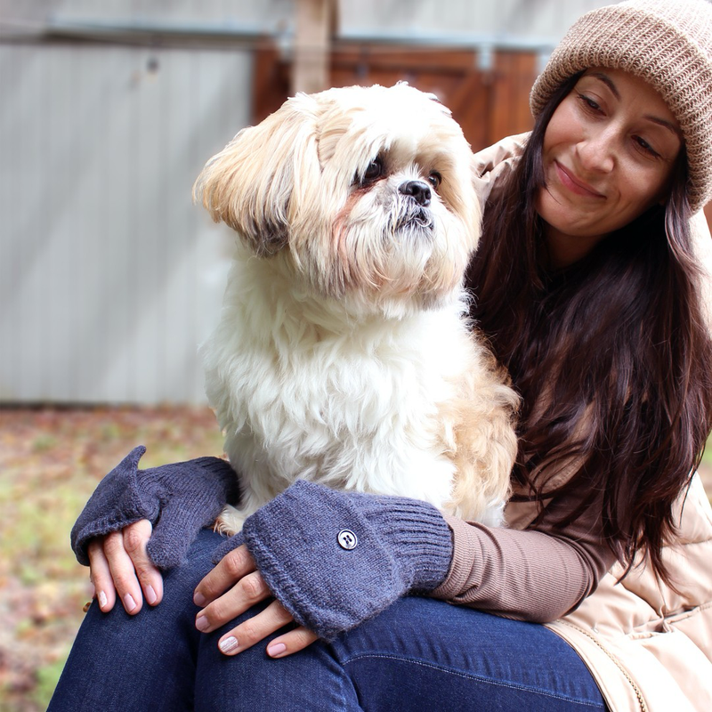 Woman holding a small dog outdoors, wearing glittens and a hat.