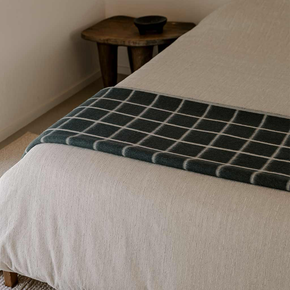Bed with a dark green checkered blanket and a wooden side table in the background.