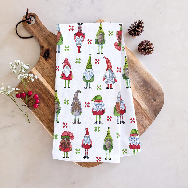 Tea towel with gnome pattern on a wooden board with pine cones and flowers.