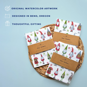 Set of tea towels with gnome design on a woven basket against a light blue background.