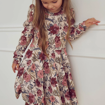 Young girl wearing a floral dress against a white wall