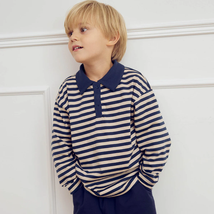 Child wearing a navy and white striped shirt with a high collar against a white wall.