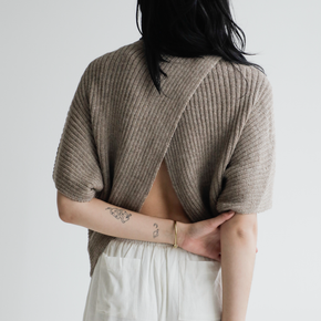 Person wearing a beige ribbed sweater over a white top on a plain background