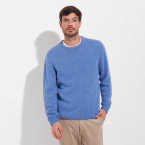 Man wearing a blue sweater and beige pants against a white background
