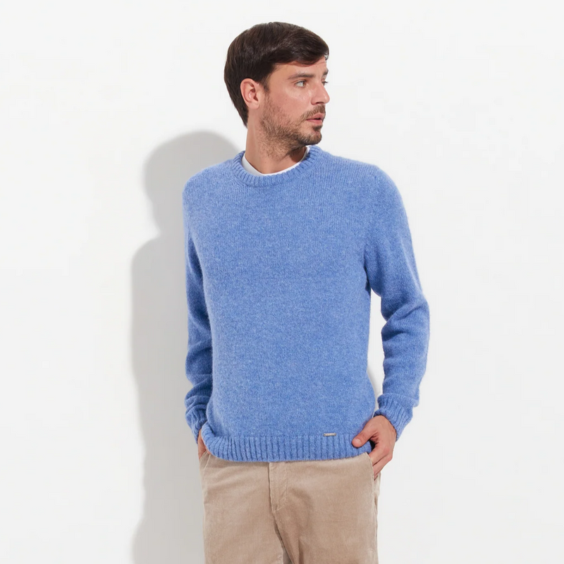 Man wearing a blue sweater and beige pants on a white background