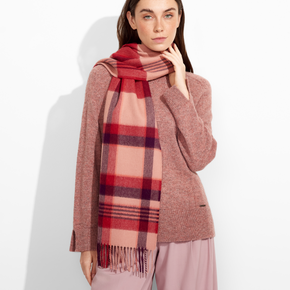 Woman wearing a red and beige plaid scarf with a pink sweater and pants on a white background