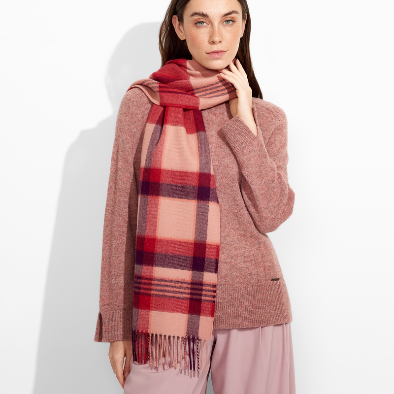 Woman wearing a red and beige plaid scarf with a pink sweater and pants on a white background