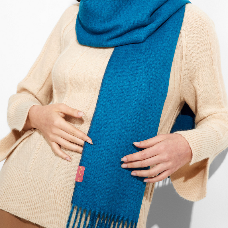 Woman wearing a blue scarf with a visible brand logo, standing against a white background