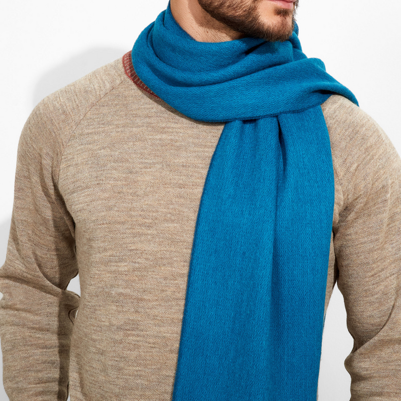 Man wearing a blue scarf and beige sweater on a white background