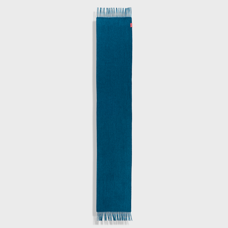 Teal scarf with white fringe on a light gray background