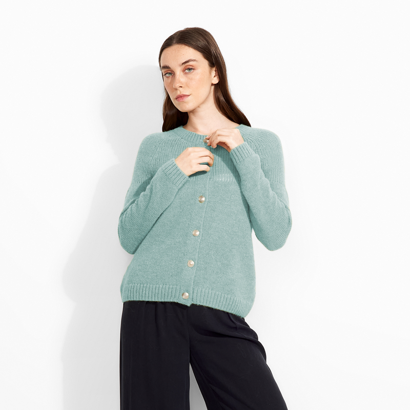 Woman wearing a light green sweater and black pants against a white background