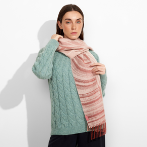 Woman wearing a green cable knit sweater and a pink scarf against a white background