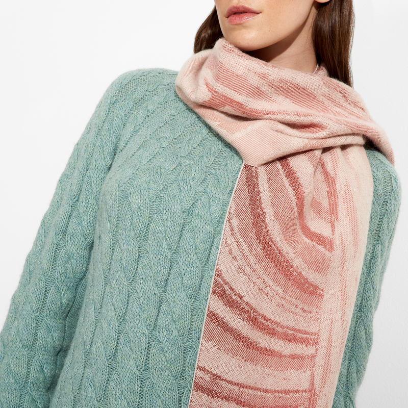 Person wearing a green cable-knit sweater and a pink scarf with red patterns on a white background