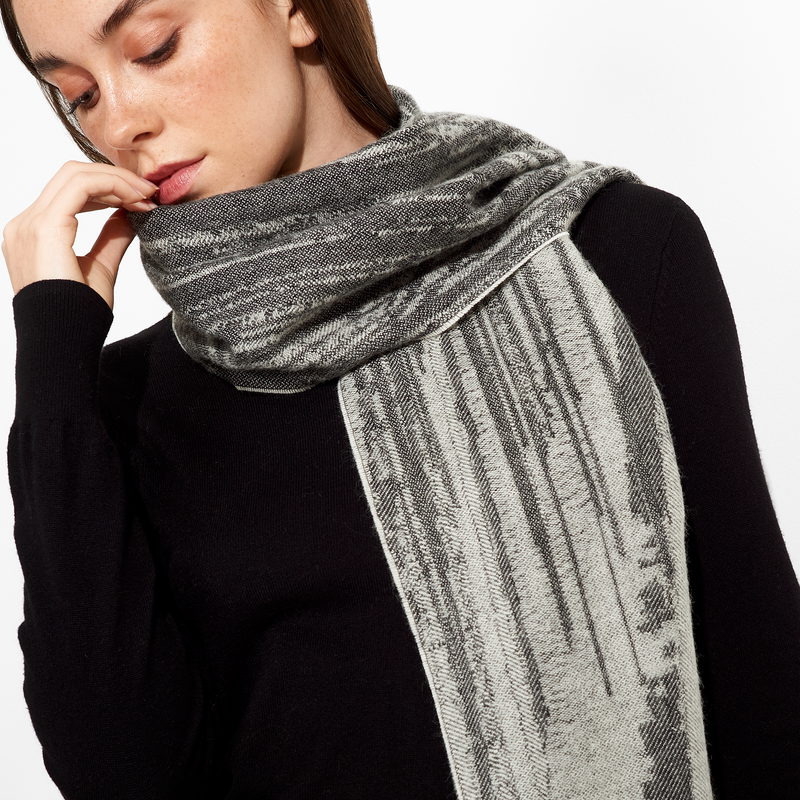 Woman wearing a gray patterned scarf with a black top on a white background