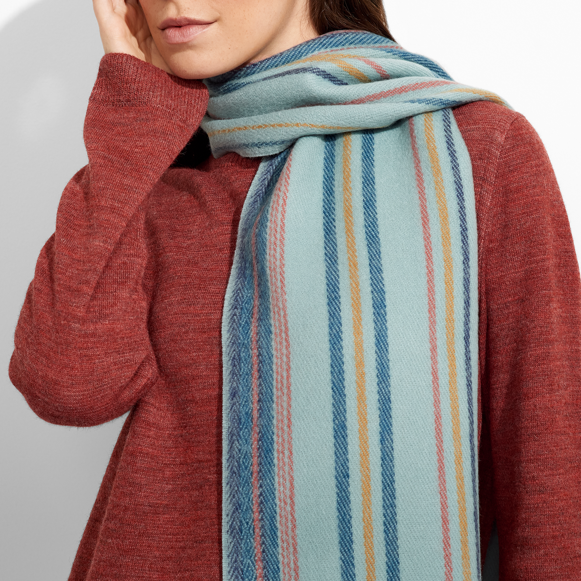 Woman wearing a red sweater and a colorful striped scarf against a plain background