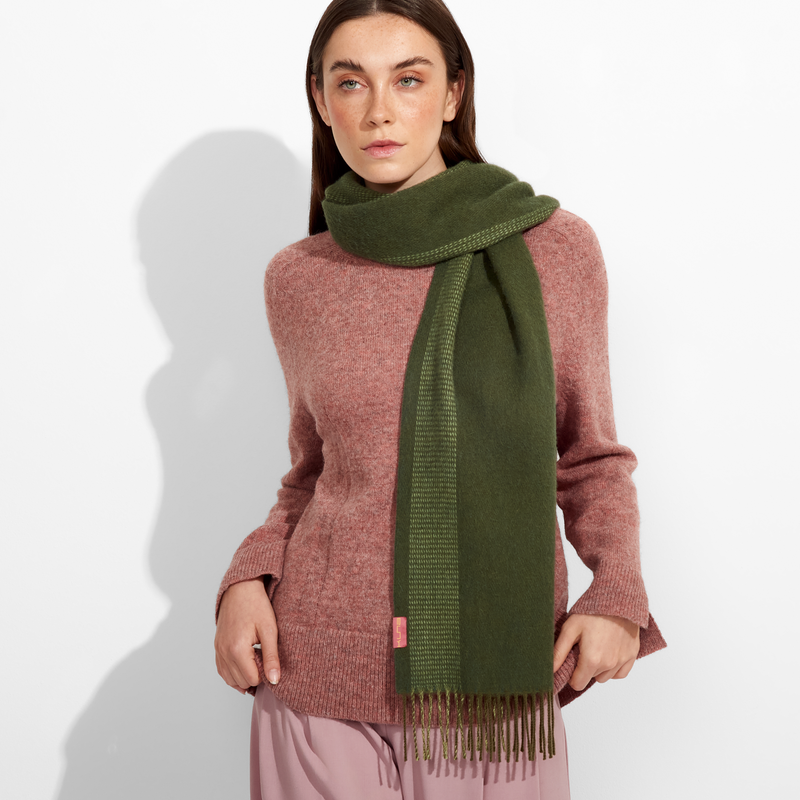 Woman wearing a pink sweater and green scarf against a white background