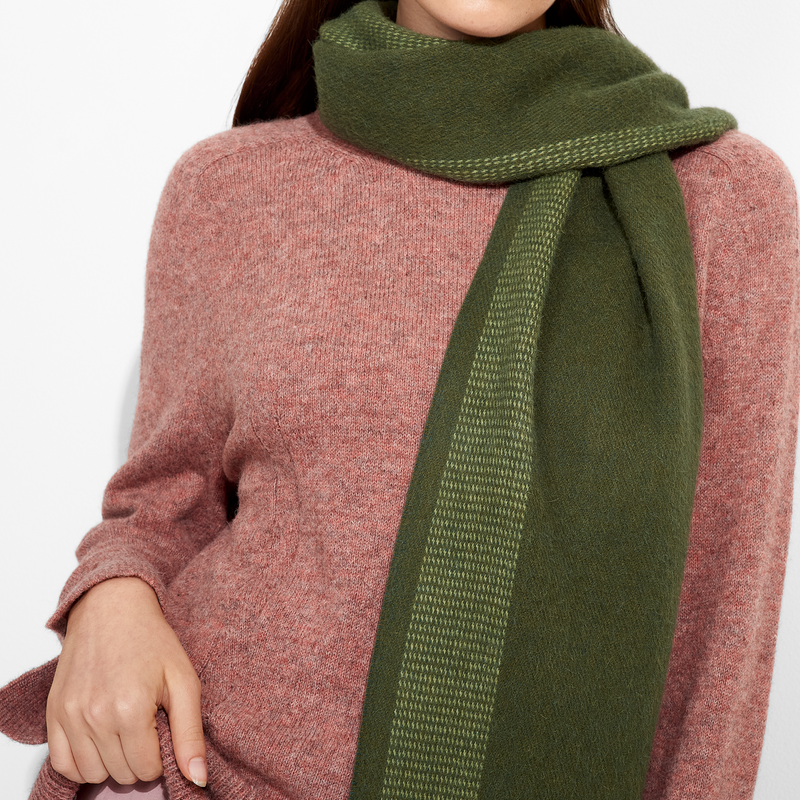 Person wearing a green scarf and pink sweater on a white background