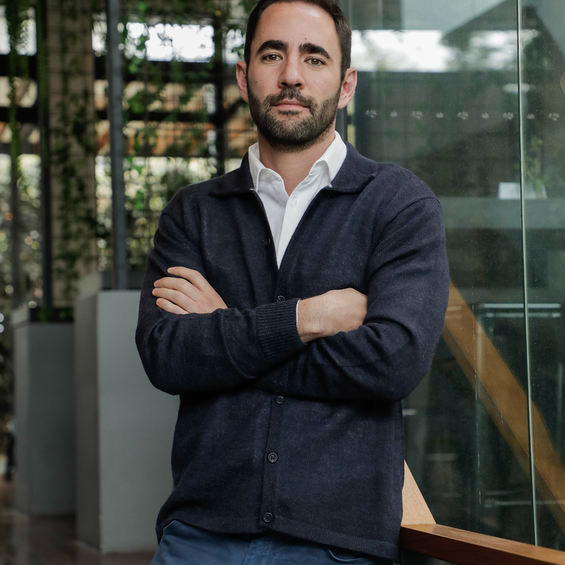 Man wearing a navy sweater over a white shirt with arms crossed, standing indoors.