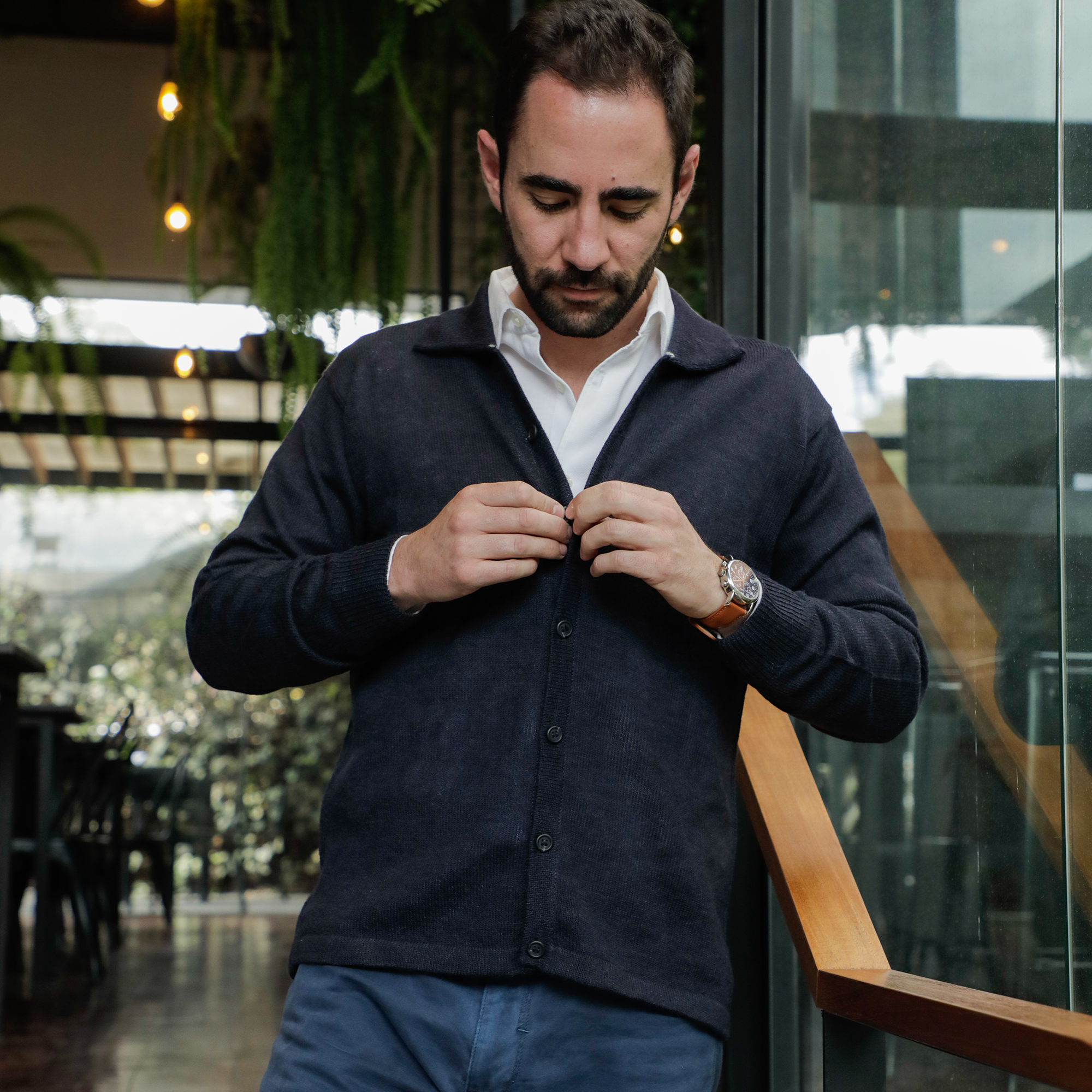 Man buttoning a dark blue shirt in an indoor setting with blurred background