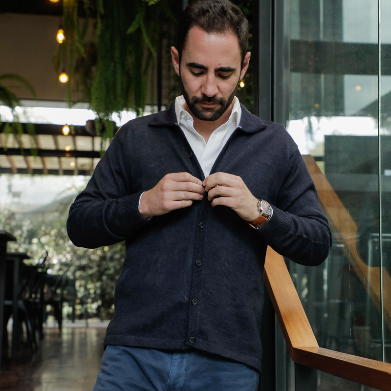 Man buttoning a dark blue shirt in an indoor setting with blurred background
