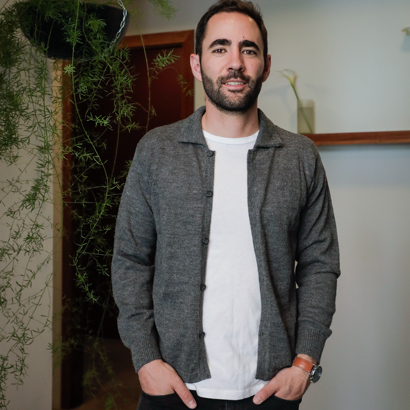Man wearing a gray cardigan over a white shirt in an indoor setting with plants.