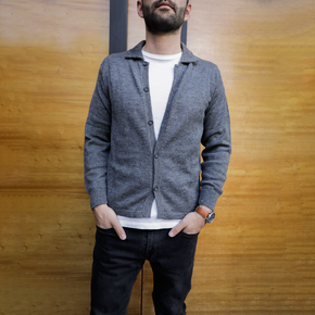 Man wearing a gray cardigan over a white shirt with a wooden background