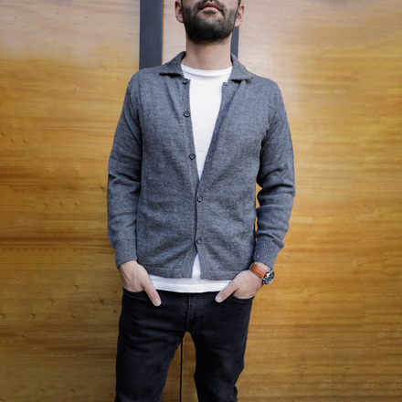 Man wearing a gray cardigan over a white shirt with a wooden background