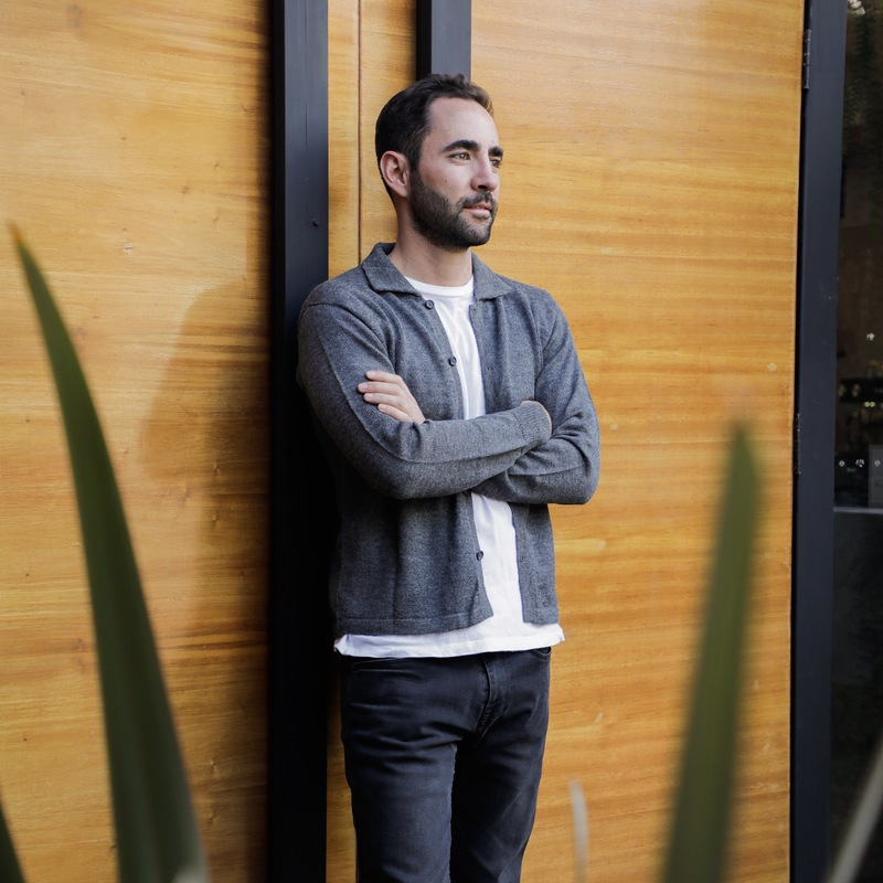 Man leaning against a wooden wall with a plant in the foreground