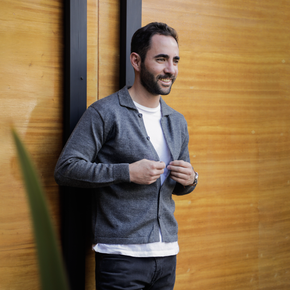 Man wearing a gray cardigan against a wooden wall