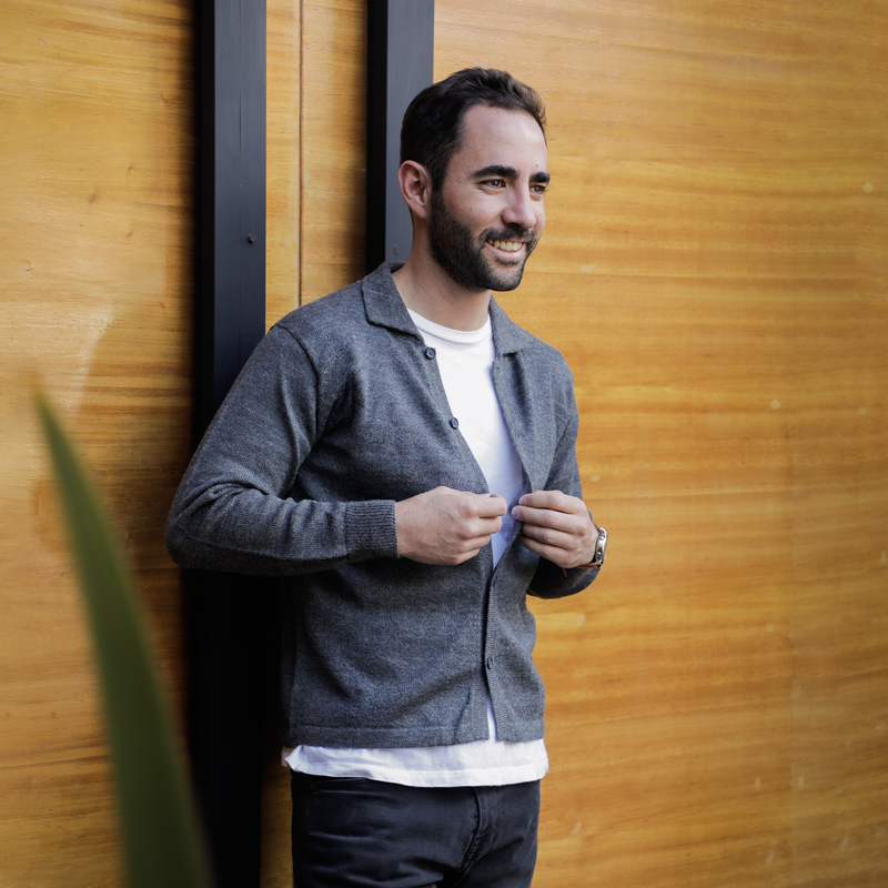 Man wearing a gray cardigan against a wooden wall