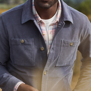 Man wearing a blue jacket with a plaid shirt underneath, standing outdoors.