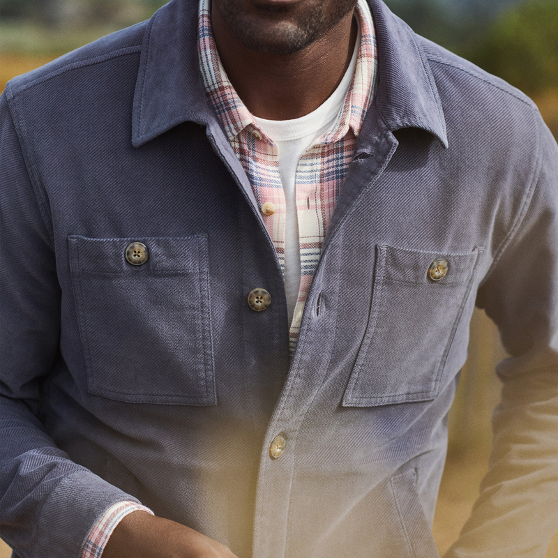 Man wearing a blue jacket with a plaid shirt underneath, standing outdoors.