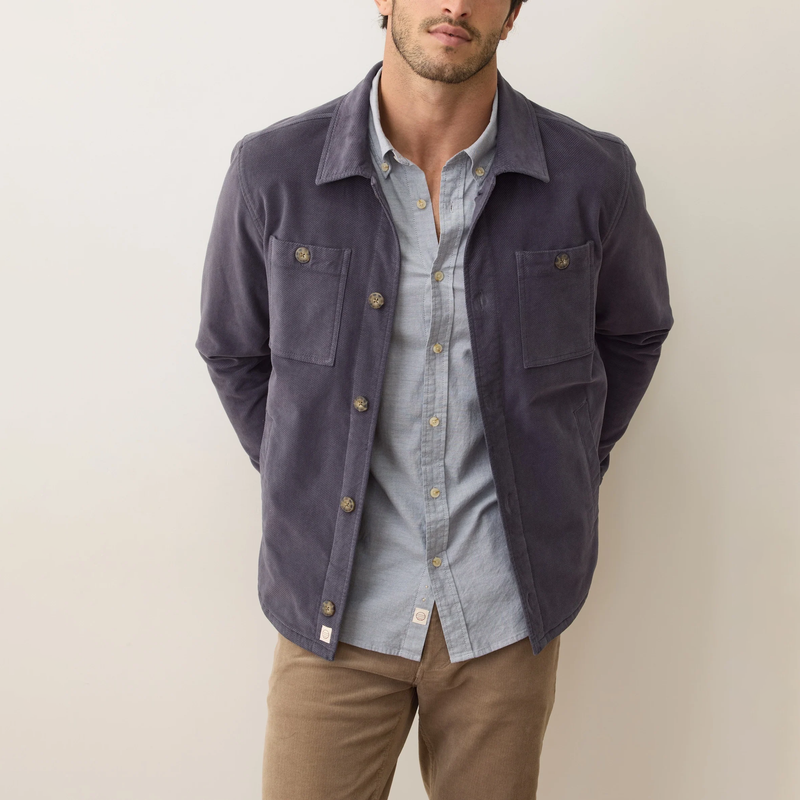 Man wearing a dark blue jacket over a light blue shirt with beige pants on a plain background