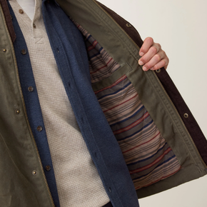 Person wearing a green jacket with a striped shirt peeking out, on a neutral background