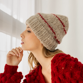 Woman wearing a beige knitted hat with red stripes and a red textured sweater.