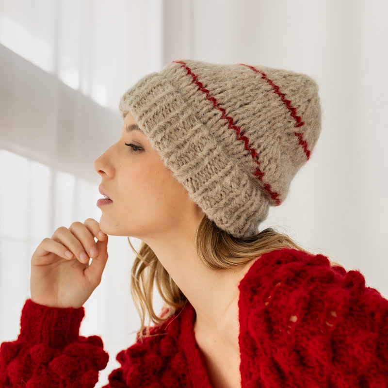 Woman wearing a beige knitted hat with red stripes and a red textured sweater.