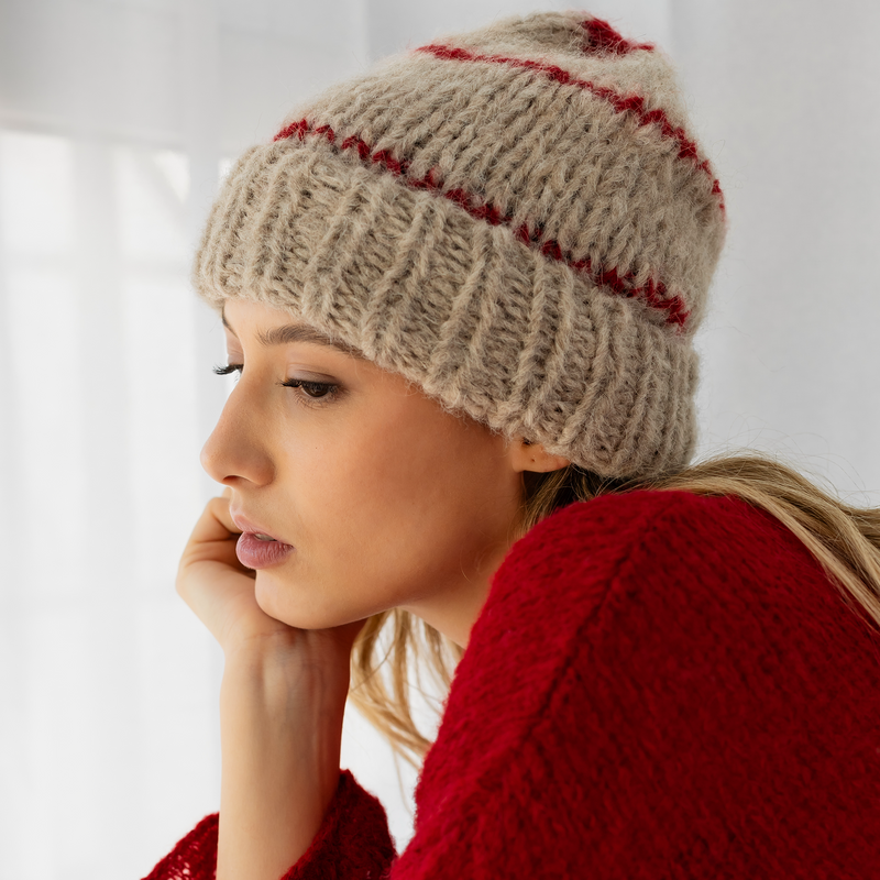 Woman wearing a beige knitted hat with red stripes and a red sweater against a white background