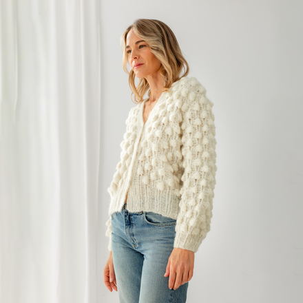 Woman wearing a white textured cardigan and blue jeans against a plain background