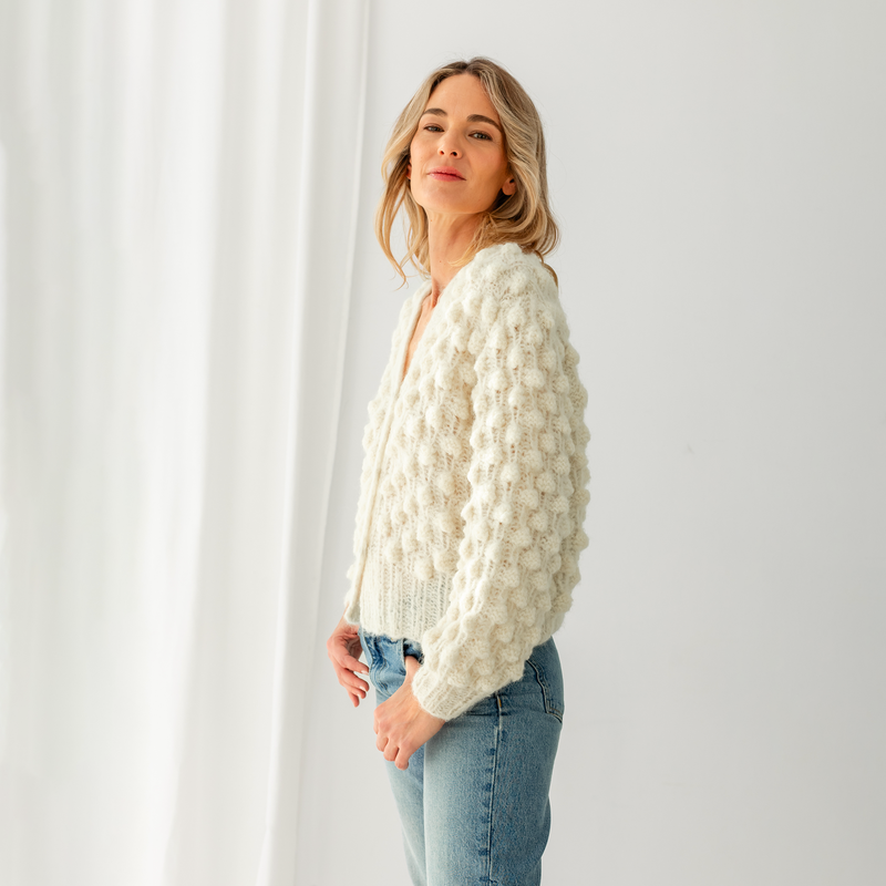 Woman wearing a white textured sweater and blue jeans against a light gray background