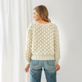 Person wearing a textured white sweater and blue jeans against a white background