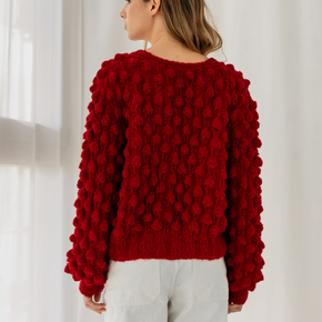 Woman wearing a red textured sweater against a white curtain background