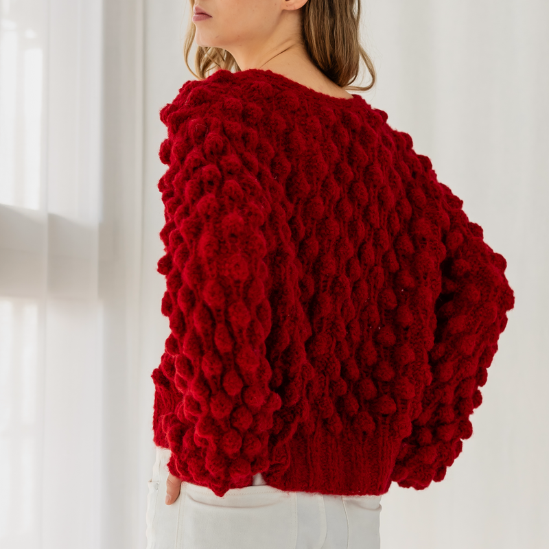 Woman wearing a red textured sweater against a white curtain background