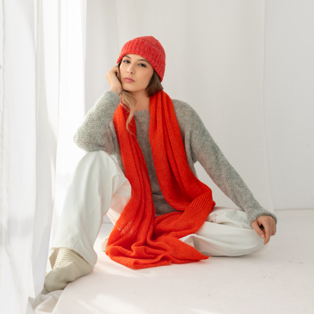 Person wearing a red shawl and hat sitting on a white surface with a white curtain in the background
