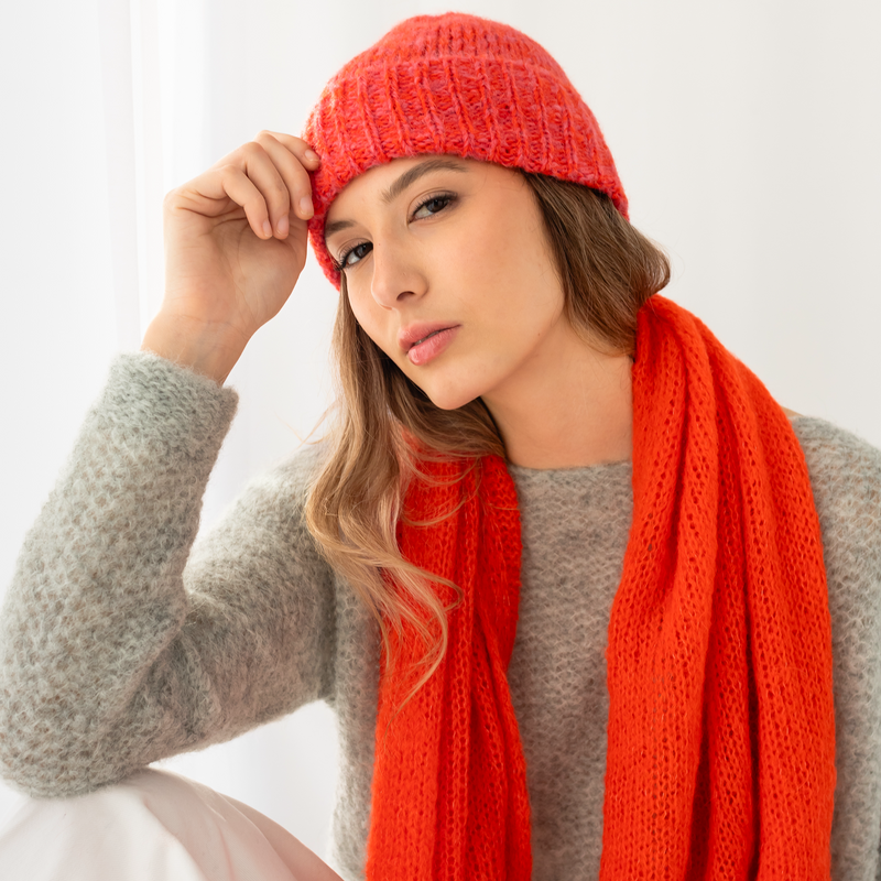 Woman wearing a red knitted hat and shawl against a white background